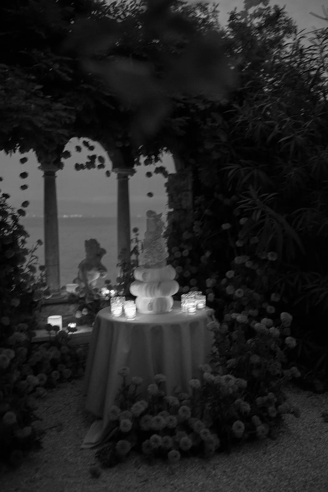 Tiered wedding cake on a candlelit table in a garden overlooking the sea at dusk