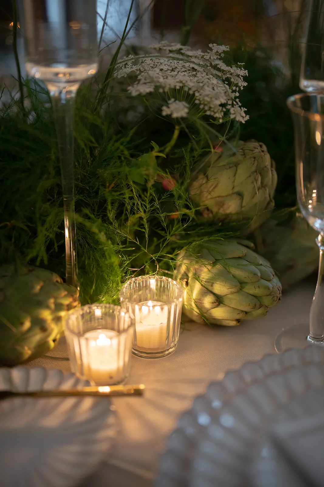 Votive candles beside artichokes, fennel and lace flowers on a set table