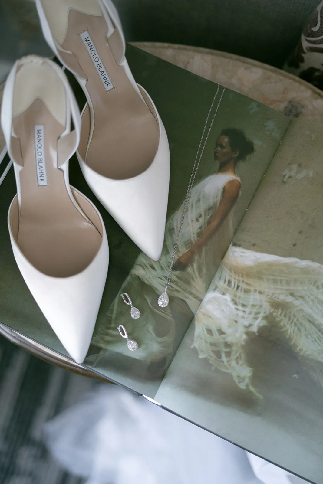 White pointed heels, diamond drop earrings and a pendant on an open book
