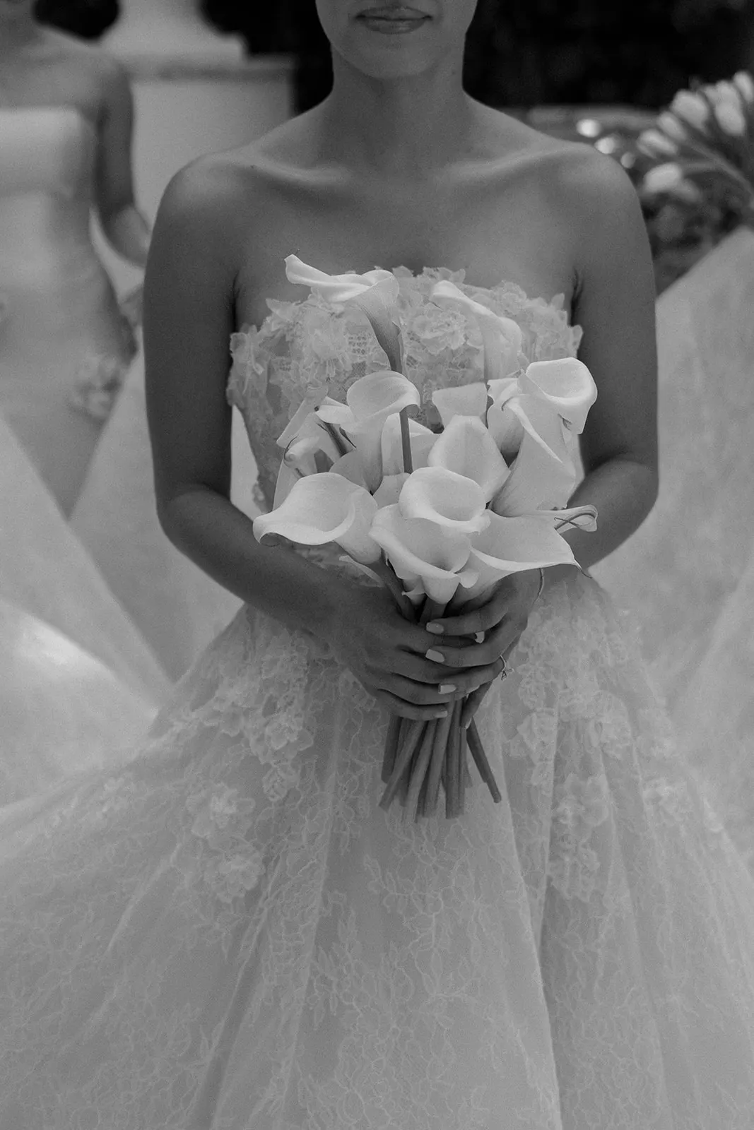 Bride in a lace gown holding a bouquet of white calla lilies, in black and white