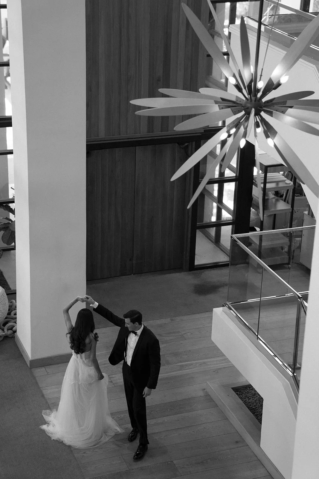 Groom twirling the bride beneath a starburst chandelier, seen from above, in black and white