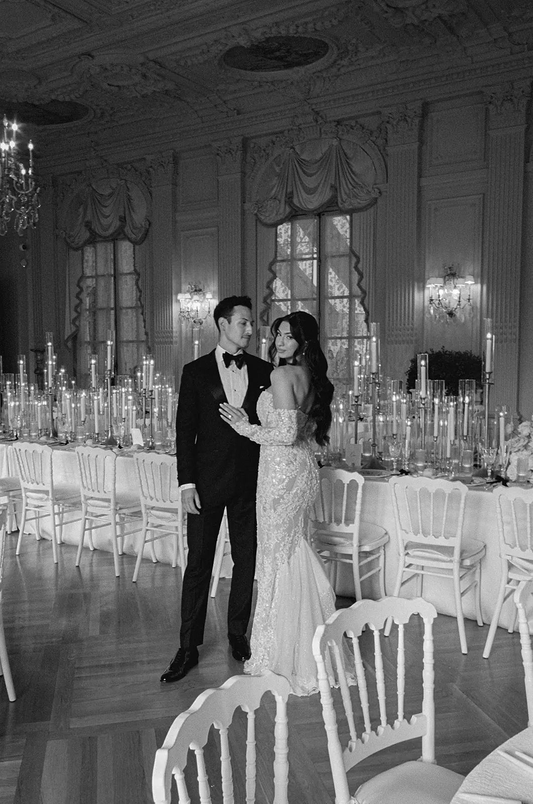 Couple embracing in a candlelit ballroom set for dinner, in black and white